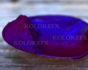 May include: A small, oval-shaped scoop containing a fine, vibrant purple powder with a metallic sheen. The powder displays deep violet and blue color shifts. The text KOLOREFX is overlaid three times across the surface of the powder.