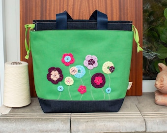 May include: A green canvas tote bag with blue denim trim and crocheted flower embellishments in pink, purple, blue, and yellow.