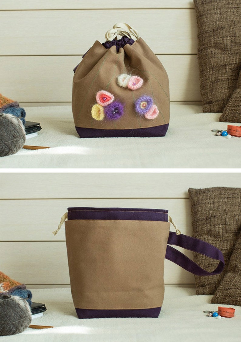 May include: A brown drawstring bag with a purple trim and crocheted flower embellishments. The bag has a purple strap.