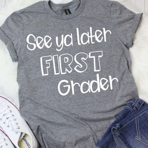 May include: Gray t-shirt with white text that reads "See ya later FIRST grader".