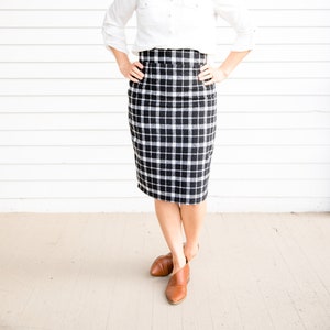 Puede incluir: Una mujer con una camisa blanca de botones, una falda lápiz de cuadros negros y blancos y zapatos de cuero marrón.