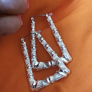 May include: A pair of silver hoop earrings with a bamboo-like design. The earrings are rectangular in shape and have a shiny finish.