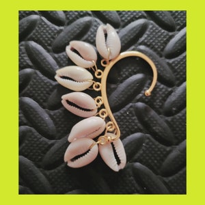 May include: Gold ear cuff with a row of small white seashells hanging from it.
