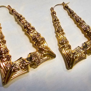 May include: A pair of large gold hoop earrings with a geometric design. The earrings are made of metal and have a shiny finish.