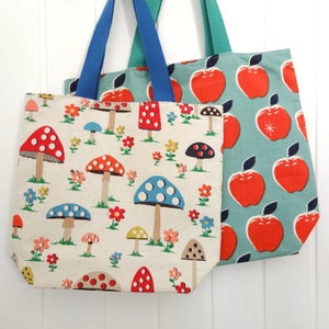 Puede incluir: Dos bolsas de tela, una con un patrón de setas azules y blancas y la otra con un patrón de manzanas rojas y verdes.