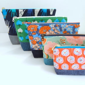 Pode incluir: Cinco bolsas com zíper coloridas com padrões diferentes. As bolsas são feitas de tecido e têm uma borda de brim. Os padrões incluem desenhos florais, geométricos e abstratos.