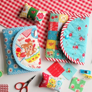 Könnte beinhalten: Vier kleine gesteppte Stoffbeutel mit verschiedenen Mustern. Die Beutel sind blau, rot und weiß mit verschiedenen Designs, darunter Pilze, Blumen und ein Comic-Mädchen. Die Beutel sind perfekt zum Aufbewahren von kleinen Gegenständen wie Nadeln, Garn oder Knöpfen.