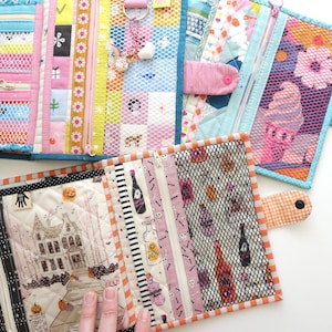K&ouml;nnte beinhalten: Eine Sammlung farbenfroher, gesteppter Stoffbeutel mit Rei&szlig;verschl&uuml;ssen und Netztaschen. Zu den Designs geh&ouml;ren Blumenmuster, Halloween-Motive mit einem Spukhaus und dekorative Streifen. Einige Beutel haben Druckkn&ouml;pfe und Anh&auml;nger.