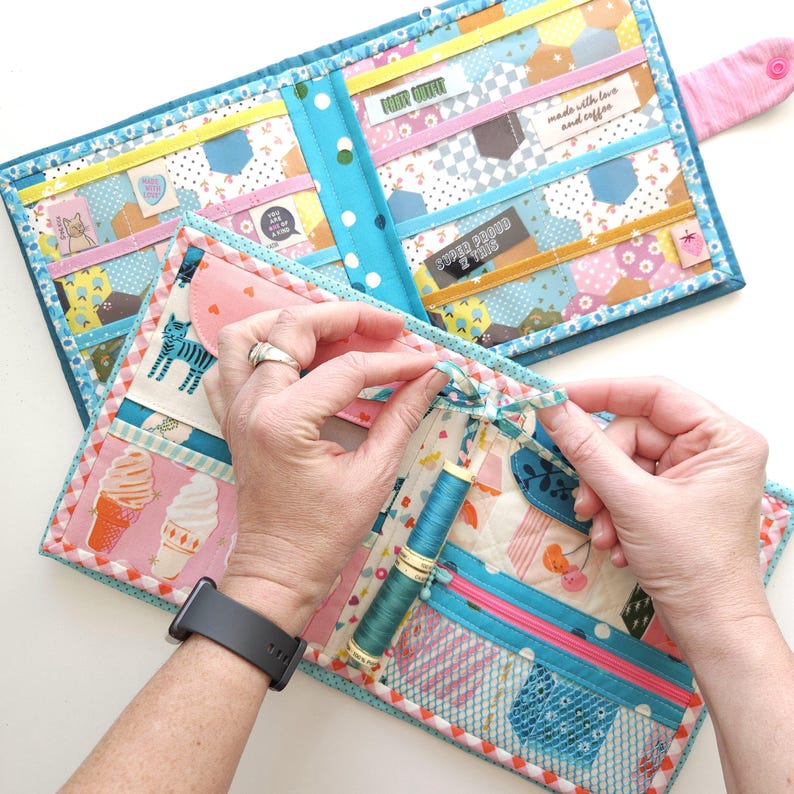 K&ouml;nnte beinhalten: Ein handgefertigter, gesteppter N&auml;h-Organizer mit farbenfrohem Patchwork-Design. Der Organizer verf&uuml;gt &uuml;ber mehrere Taschen, einen Rei&szlig;verschluss und eine Spule mit teal-farbenem Faden. Das Innere hat verschiedene Stoffmuster, darunter Eiswaffeln und ein Zebra.