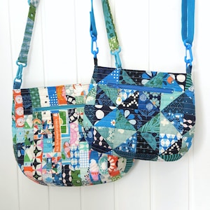 Op de afbeelding: Twee patchwork crossbody-tassen van stof met blauwe en groene geometrische patronen. De grotere tas heeft een ritsvak en een regenboogkleurig stoffen detail. De kleinere tas heeft een ritsvak en een blauw en groen bloemenstof detail.