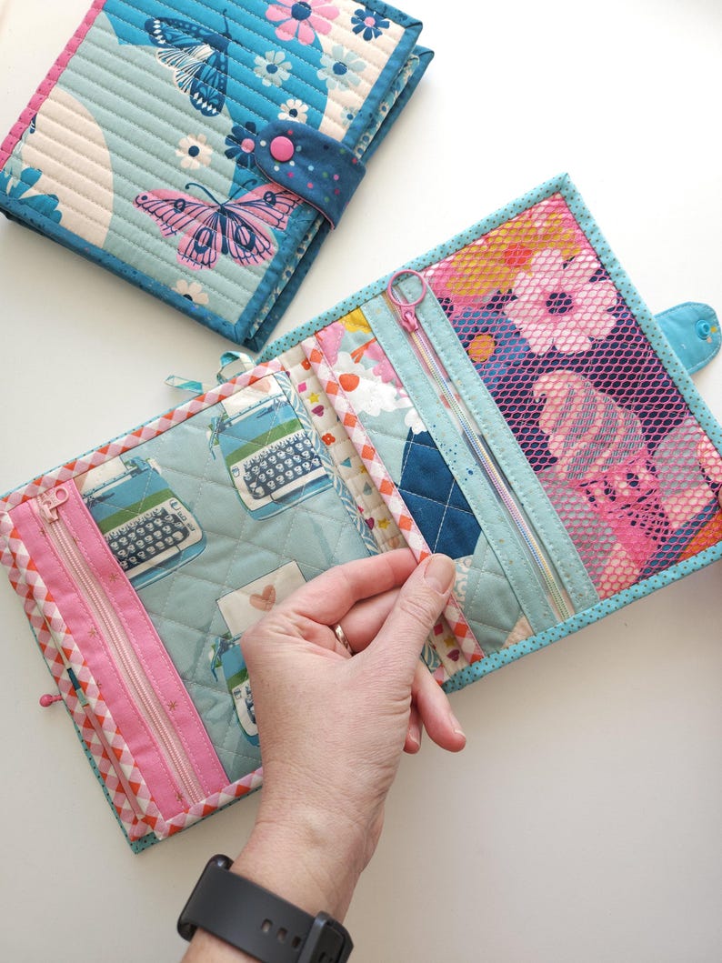 K&ouml;nnte beinhalten: Quilt-Organizer aus Stoff mit einem Schmetterlings- und Blumenmuster. Der Organizer hat mehrere F&auml;cher, darunter Rei&szlig;verschlusstaschen. Das Farbschema umfasst Blau-, Rosa- und Wei&szlig;t&ouml;ne. Der Organizer ist f&uuml;r die Aufbewahrung kleiner Gegenst&auml;nde konzipiert.
