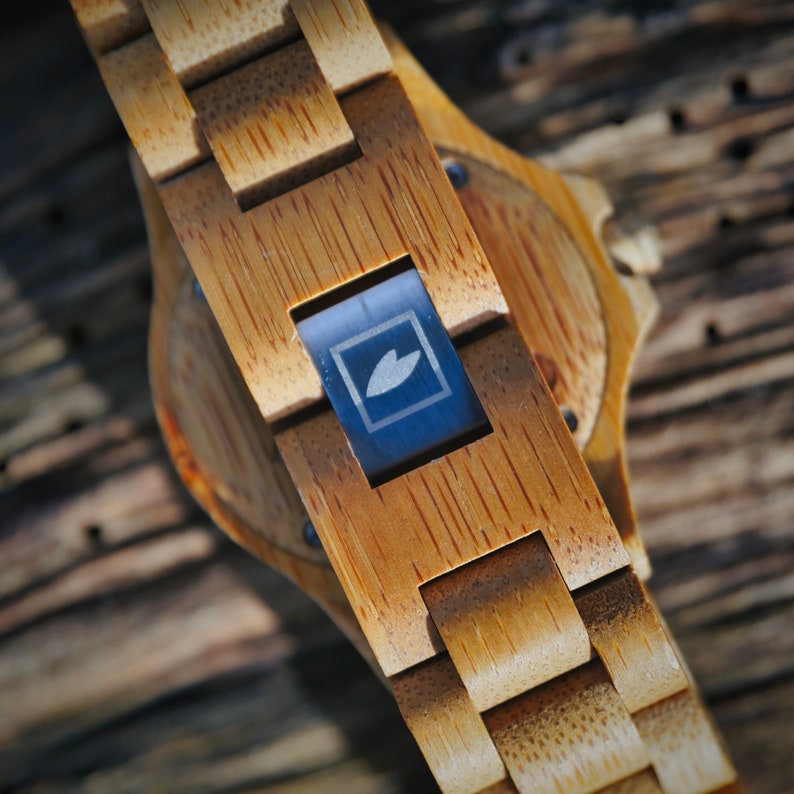 May include: A wooden wristwatch with a brown bamboo band and a dark blue face with a leaf logo.