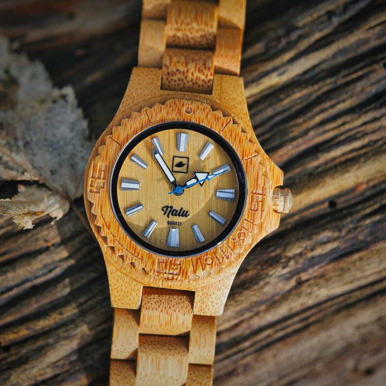 May include: A wooden wristwatch with a light brown bamboo band and a round face. The face has white markings and a blue second hand. The watch face says "Nalu Quartz".