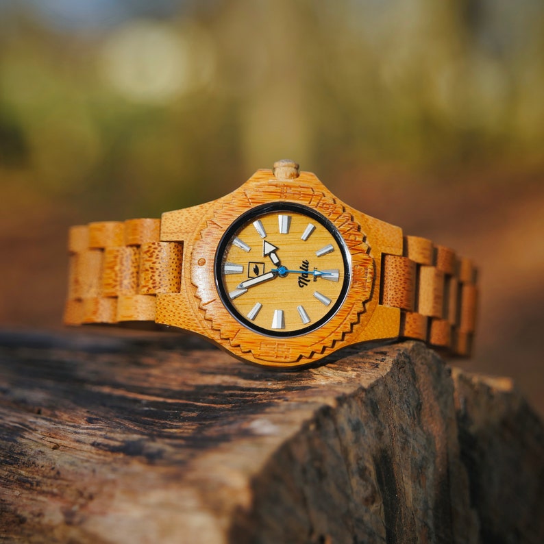 May include: A wooden wristwatch with a light brown bamboo band and a round, white face with black markings. The watch face has a small leaf icon and the word "Talu" printed on it.