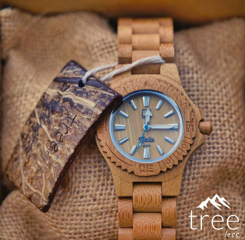May include: A wooden wristwatch with a brown wooden band and a light brown face. The watch face has a blue second hand and the words "Jalu" and "QUARTZ" printed on it. The watch is sitting on a brown burlap surface. The text "tree less" is printed in white on a black background in the lower right corner of the image.