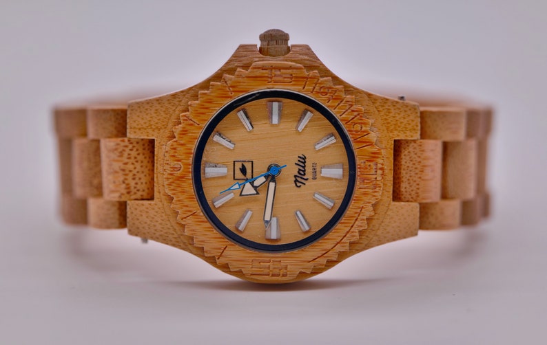 May include: A wooden wristwatch with a light brown bamboo band and a cream-colored face. The watch face has black markings and a blue second hand. The watch face also has the word "Malu" printed on it.