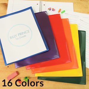 May include: A set of 10 colorful plastic folders with a clear front pocket. The folders are arranged in a rainbow pattern, with the blue folder on top and the green folder on the bottom. The folders are labeled with the text "Billy Prince 1st Grade".