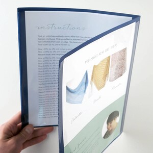 May include: A blue plastic folder with a white sheet inside. The sheet has the word "instructions" written in cursive at the top and knitting instructions below. The right side of the folder has a white sheet with the text "YOU MIGHT ALSO LIKE THESE" and pictures of three different shawls.