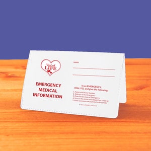 May include: White card with a red heart logo that says "Vial of Life". The card has a section for names and a section for emergency medical information. The text says "In an emergency, dial 911 and give the following: 1. Name and phone number 2. Address of the emergency 3. Describe the type of emergency 4. Stay on the phone until dispatcher hangs up 5. Have someone wait outside to direct help".