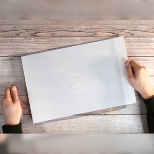 May include: A white sheet of paper is being placed into a clear plastic document protector. The protector has a white border around the edges.
