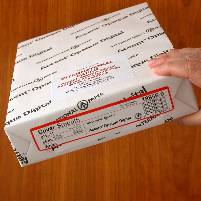 K&ouml;nnte beinhalten: Eine wei&szlig;e Schachtel mit Accent Opaque Digital Cover Smooth Papier. Die Schachtel ist mit dem Produktnamen, der Gr&ouml;&szlig;e, dem Gewicht und der Menge beschriftet. Die Schachtel hat auch einen Barcode und den Text "International Paper" aufgedruckt.