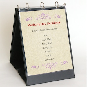 May include: A black binder with a clear plastic cover displaying a sign for Mother's Day Necklaces. The sign lists the following colors: Aqua, Light Blue, Navy Blue, Turquoise, Scarlet, Coral, and Lavender.