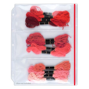 May include: A clear plastic floss organizer with three sections, each holding several bundles of red, pink, and coral embroidery floss. The organizer has a red vertical stripe on the right side and the text "Floss not included" at the bottom.