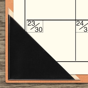 May include: Close-up of a calendar page corner with a black leather-like corner protector. The calendar grid is cream-colored with black lines. The date boxes show the numbers 23/30 and 24/30.