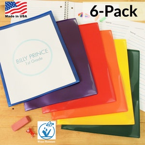 May include: A six-pack of clear plastic folders with colorful borders. The folders are water-resistant and have a label area for writing names. The folders are stacked in a rainbow pattern, with the blue folder on top and the green folder on the bottom.