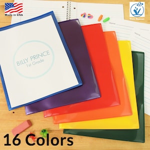 May include: A set of 16 colorful plastic folders with a blue folder on top. The blue folder has a white label with the text "BILLY PRINCE 1st Grade". The folders are water resistant and made in the USA.