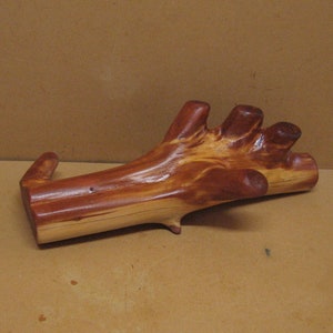 May include: A natural wood branch with a unique shape, resembling a hand. The branch is polished and has a reddish-brown color with a light wood grain.