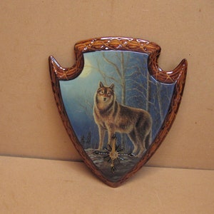 May include: A wooden wall plaque shaped like an arrowhead with a painted image of a wolf in a forest setting under a full moon.