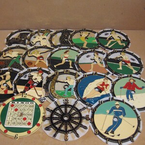 May include: A collection of 17 round, colorful, painted wooden clock faces with various sports themes. Each clock face features a different sport, including wrestling, hockey, skiing, swimming, and running. The clock faces are arranged in a circle, with a bingo card in the center.