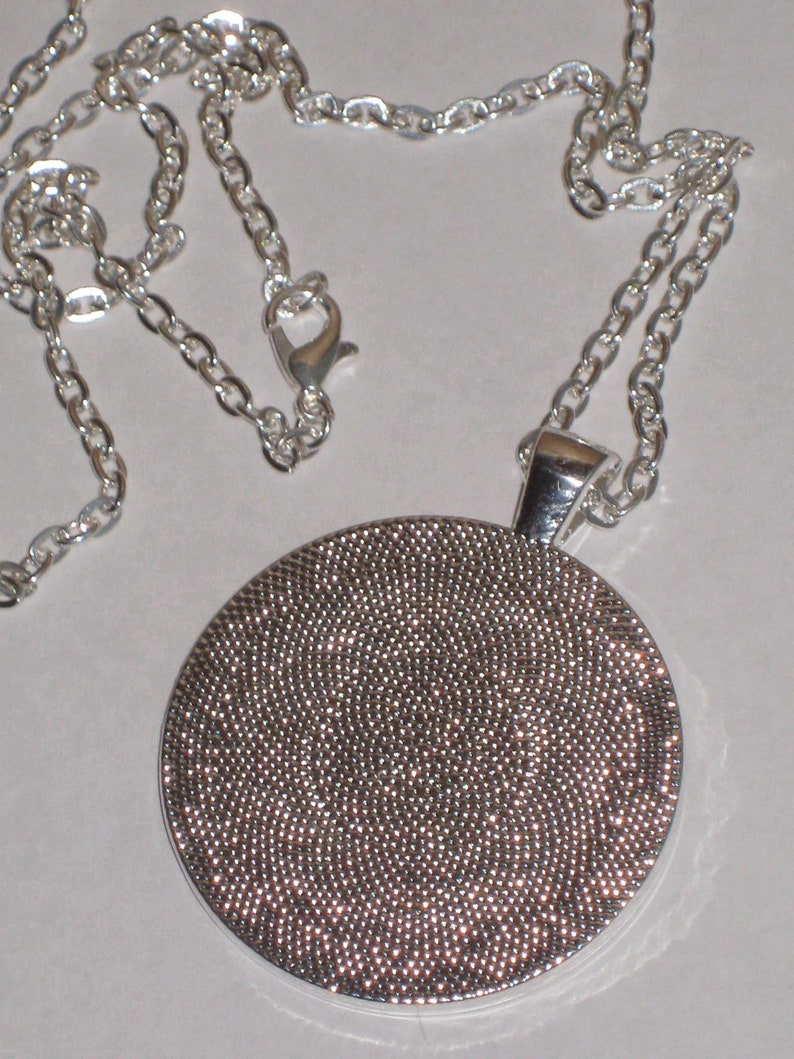 May include: A silver chain necklace with a round pendant. The pendant is covered in small, silver dots.