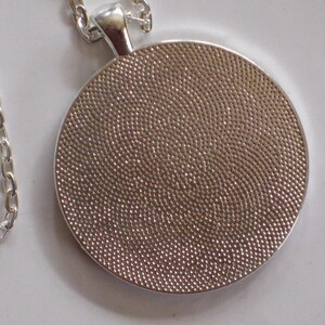 Puede incluir: Collar de cadena de plata con un colgante redondo. El colgante tiene una superficie texturizada.