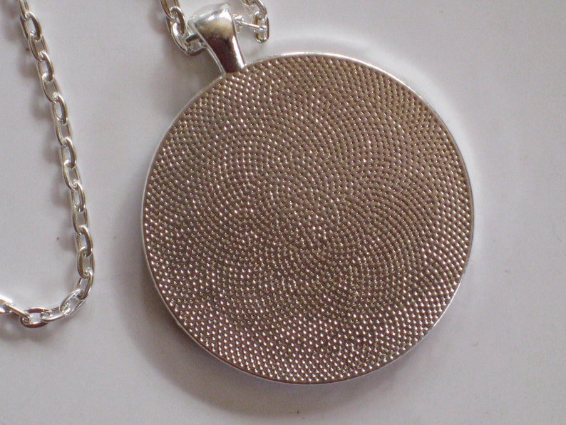 Puede incluir: Collar de cadena de plata con un colgante redondo. El colgante tiene una superficie texturizada.