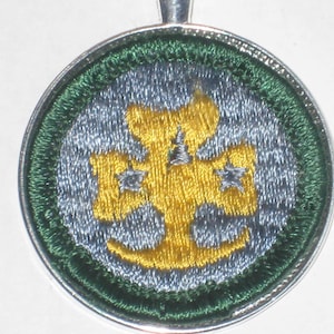May include: A silver and green round patch with a yellow embroidered four-leaf clover with three stars.