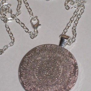 May include: A silver chain necklace with a round pendant. The pendant is covered in small, silver dots.