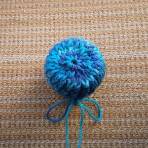 May include: A blue and teal yarn pom-pom with a knotted string attached.