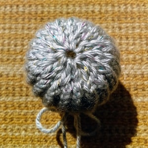 May include: A gray crocheted ball with a hole in the center and a white string attached.