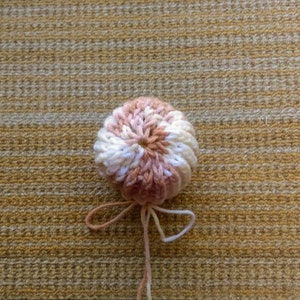 May include: A pink and white crocheted ball with a long string attached. The ball is on a brown and white striped surface.