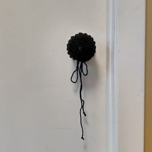 May include: A black crocheted pom-pom with a long black string hanging from it.