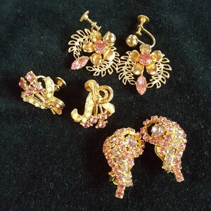 May include: Set of five pairs of vintage earrings with pink rhinestones. The earrings are made of gold-tone metal and feature a variety of designs, including floral, geometric, and abstract.