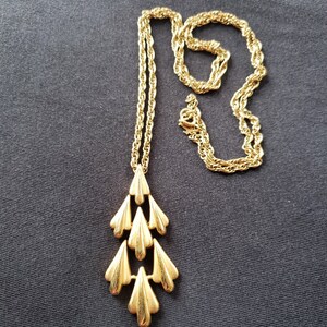 Pu&ograve; includere: Una collana dorata con un pendente a cascata a forma di foglie. La catena &egrave; a corda intrecciata e il pendente presenta molteplici forme di foglie stilizzate a strati. La collana &egrave; esposta su uno sfondo di tessuto grigio scuro.