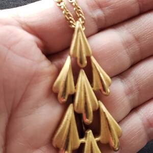 Pu&ograve; includere: Collana dorata con una cascata di pendenti stilizzati a forma di foglia. La catena e i pendenti hanno una finitura lucida, creando un'estetica vintage. La collana &egrave; esposta su uno sfondo neutro.