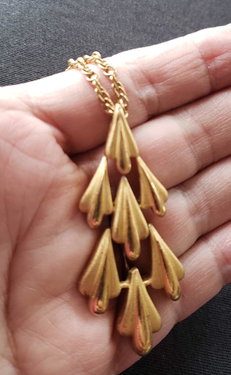Pu&ograve; includere: Collana dorata con una cascata di pendenti stilizzati a forma di foglia. La catena e i pendenti hanno una finitura lucida, creando un'estetica vintage. La collana &egrave; esposta su uno sfondo neutro.