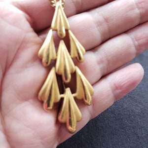 Pu&ograve; includere: Una collana con pendente dorato con un design a cascata di elementi stilizzati a forma di ventaglio. La collana ha una catena delicata e una finitura lucida, creando un'estetica vintage. Il design del pendente &egrave; simmetrico e accattivante.