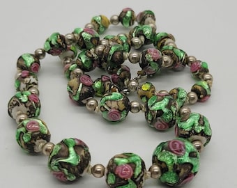 May include: A vintage necklace with large, round beads in a mix of colours. The beads have a brown base with green, pink, and yellow accents. Small, silver-coloured beads separate the larger beads, creating a unique jewellery piece.