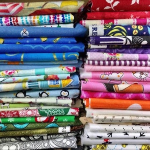 May include: A stack of colorful fabric squares with various patterns, including penguins, birds, flowers, and geometric designs. The fabrics are arranged in a vertical stack, with the top of the stack on the left side of the image.