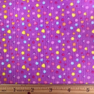 May include: Purple fabric with a repeating pattern of small yellow, pink, blue, and orange shapes. A ruler is included in the image with markings from 1 to 5 inches.